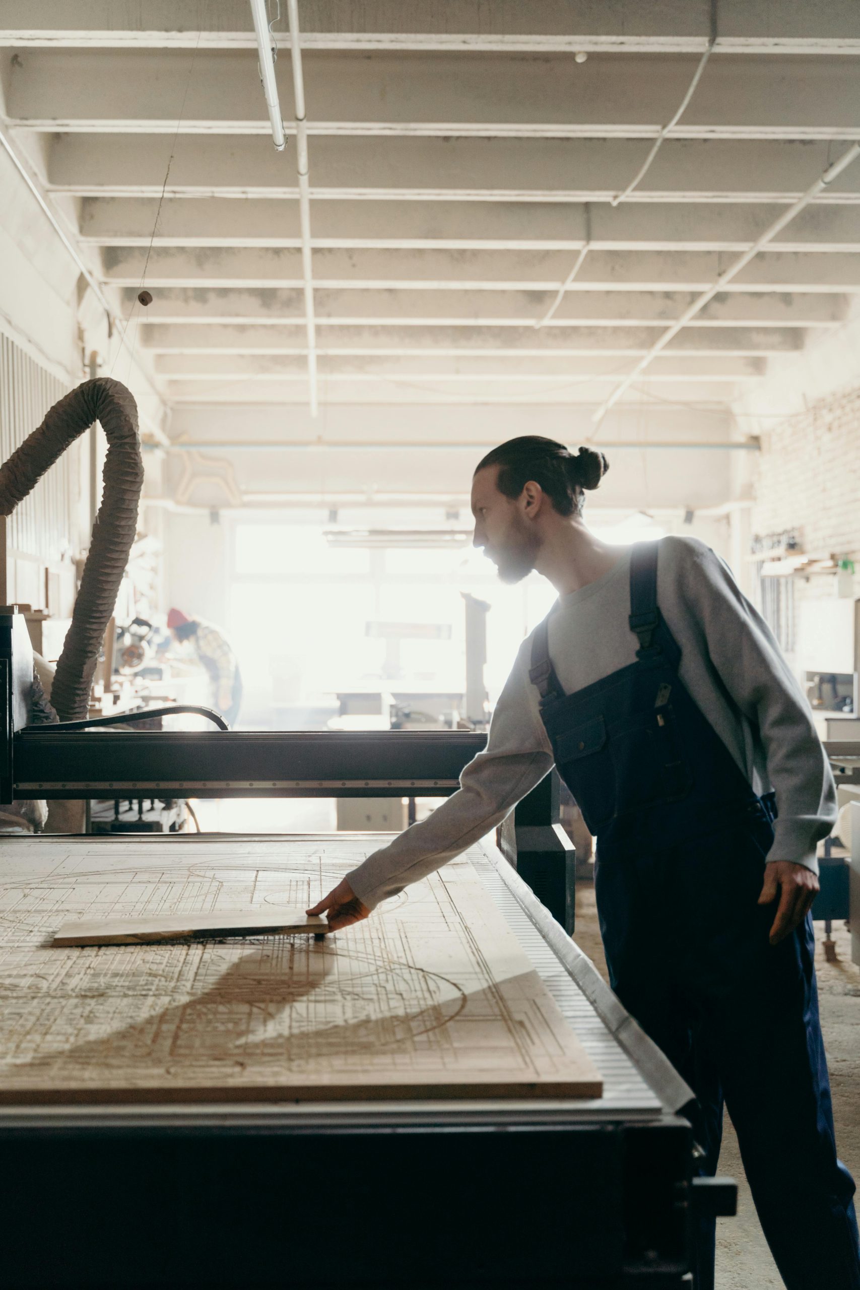 Craftsman measuring wood in a well-lit industrial workshop.