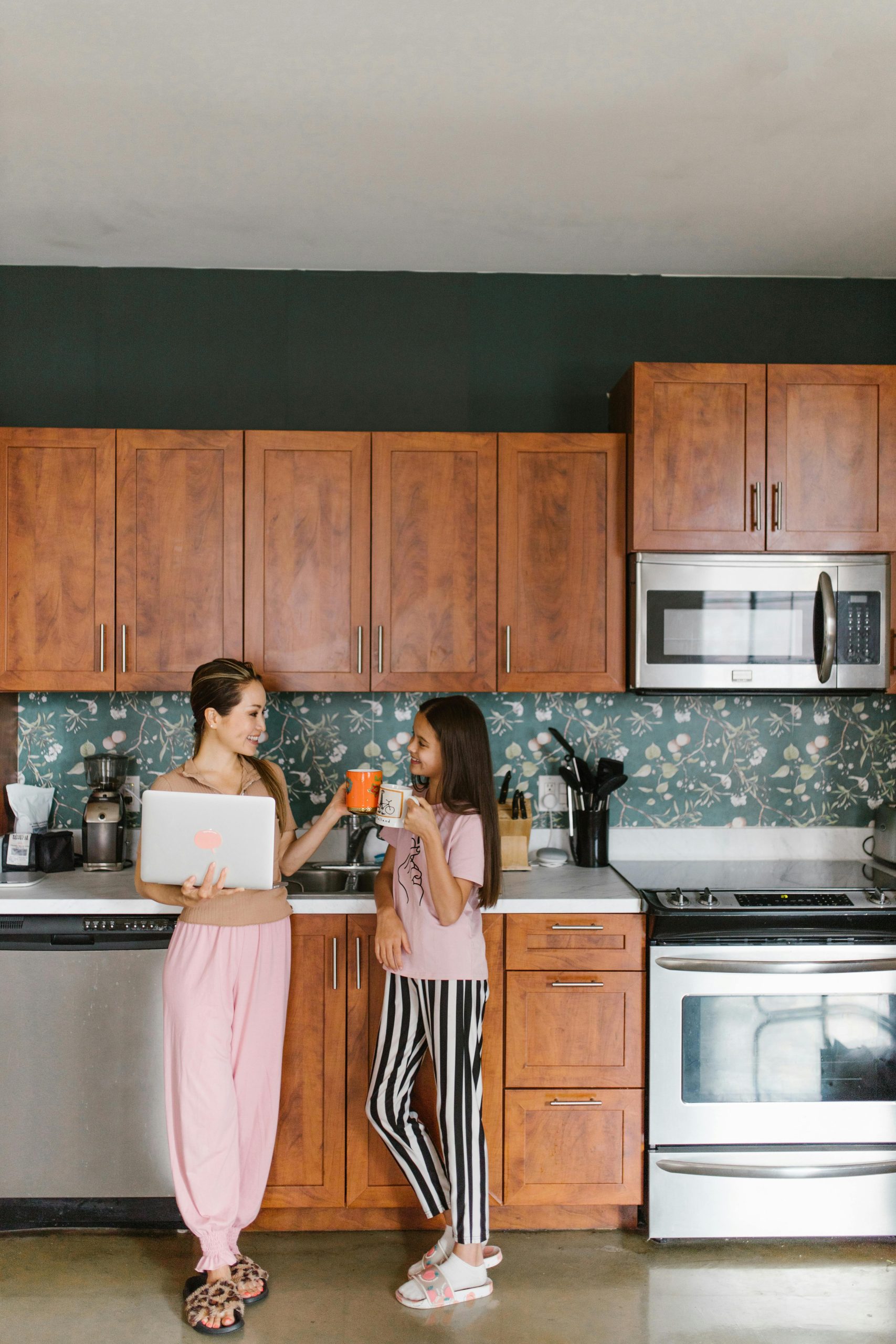 Mother and daughter sharing a moment in modern kitchen, engaging with laptop.